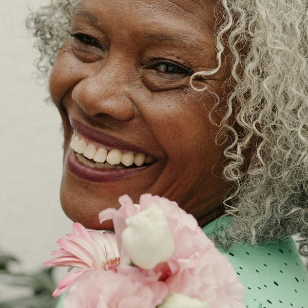 Close-up of a joyful senior woman with silver hair holding pink flowers, representing the vibrant and enriching coastal lifestyle