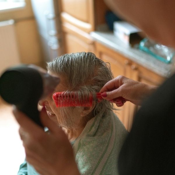 A caregiver providing personalized grooming and hair care for a resident, highlighting the 1:5 staff-to-resident ratio and attentive support.